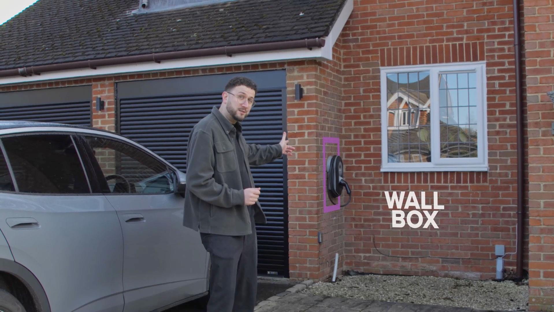 EV expert stands outside house with electric car and EV wall charger