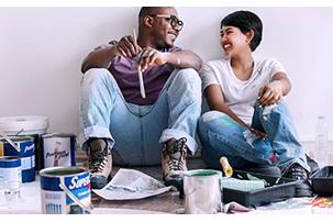 Man and woman laughing surrounded by house painting materials