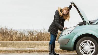 Woman looking inside the bonnet of her car by the side of the road