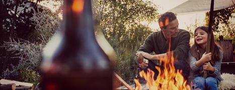 Father and daughter sit in garden in front of a fire pit