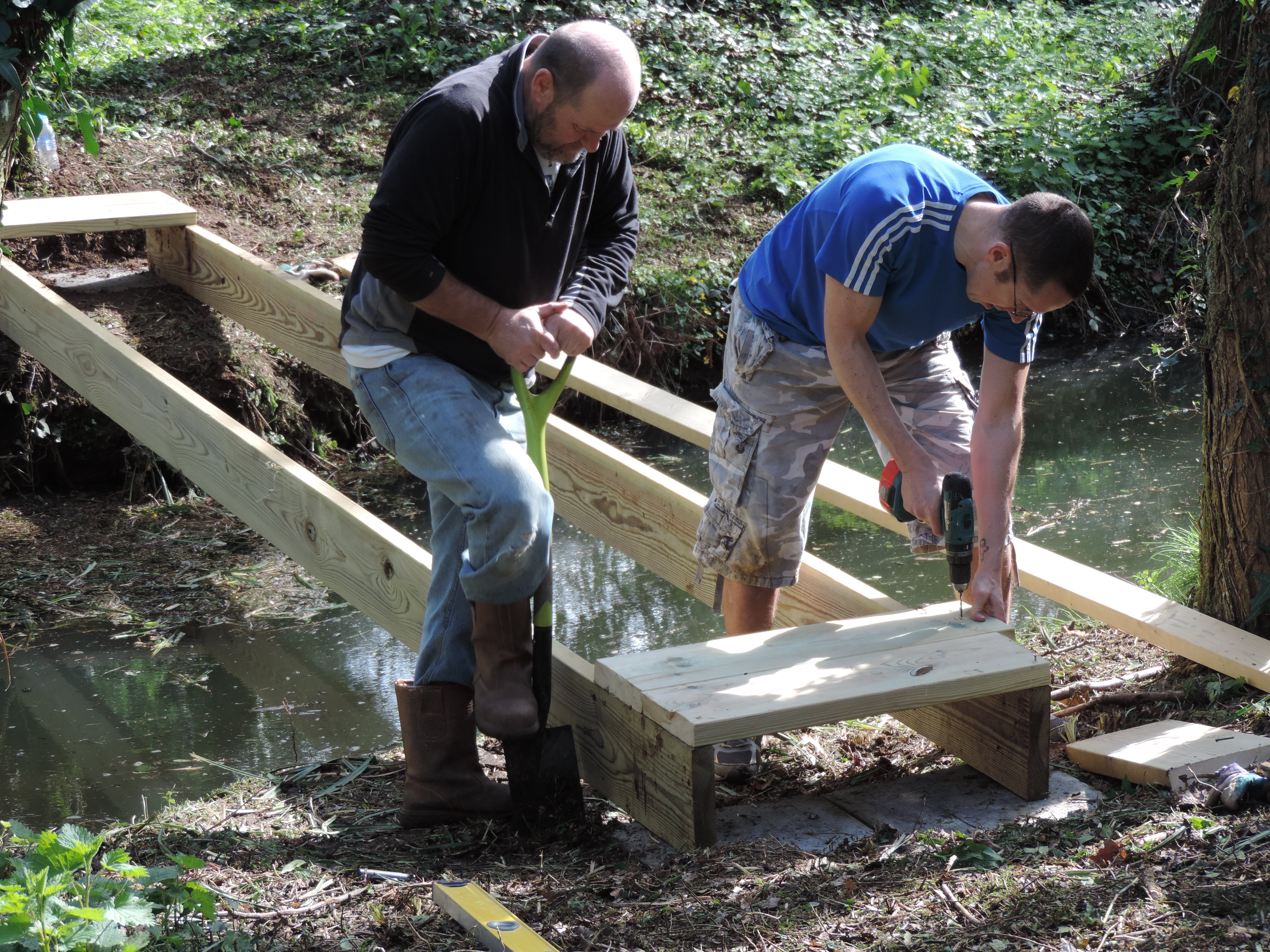 Two men building a bridge over a lake