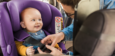 Parent buckling their newborn baby in a car seat