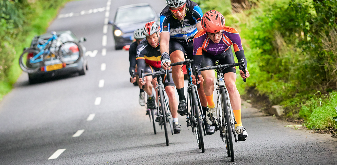 group of cyclists on the road with a car approaching behind