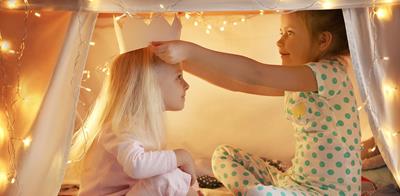 two children playing indoors in a makeshift fort