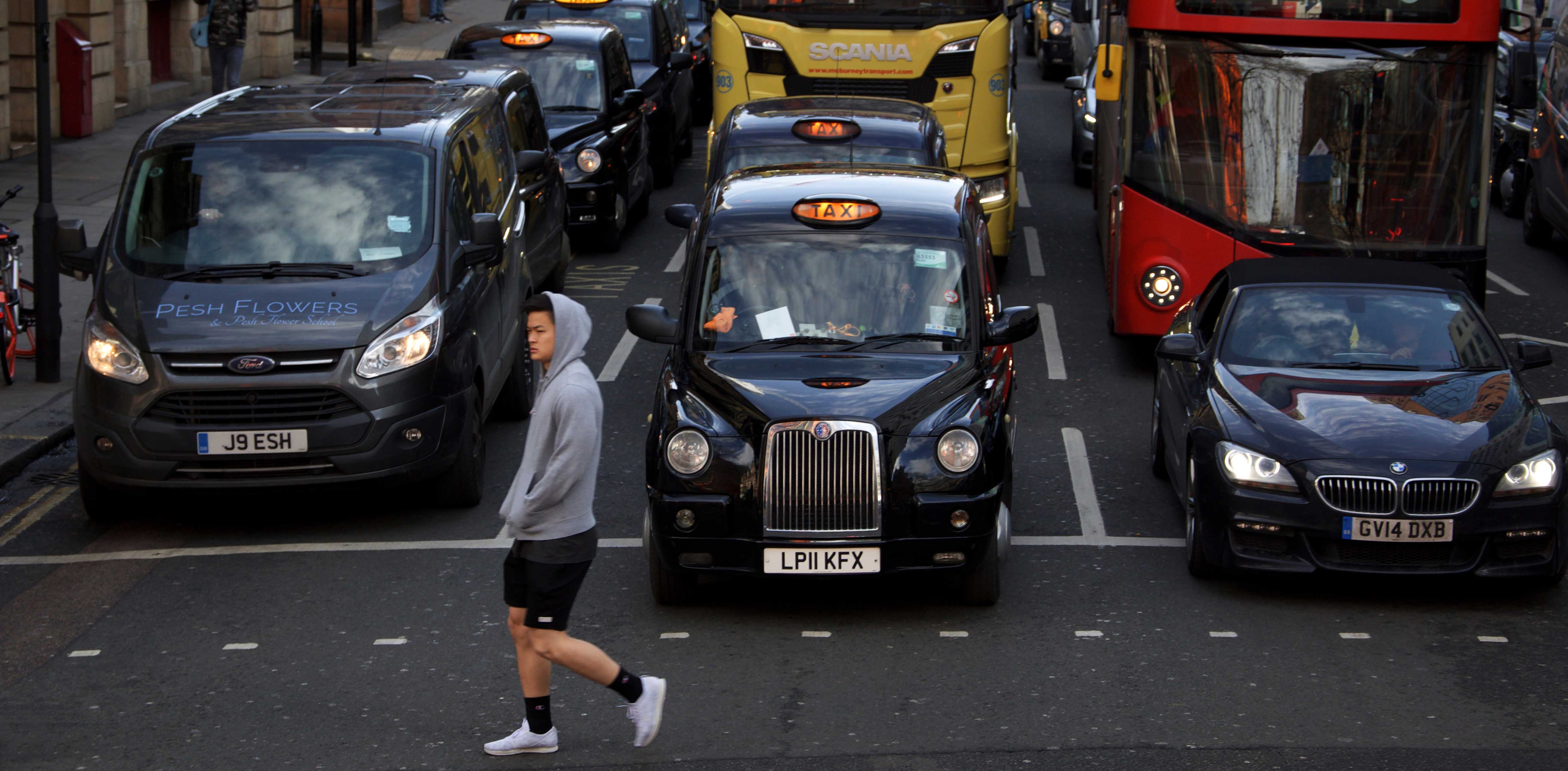 Man walking past London traffic taxis cars and buses