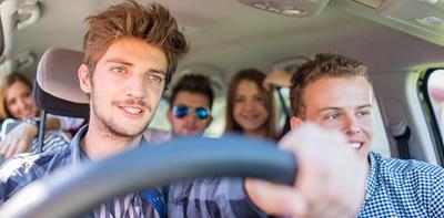 young man driving car with friends as passengers